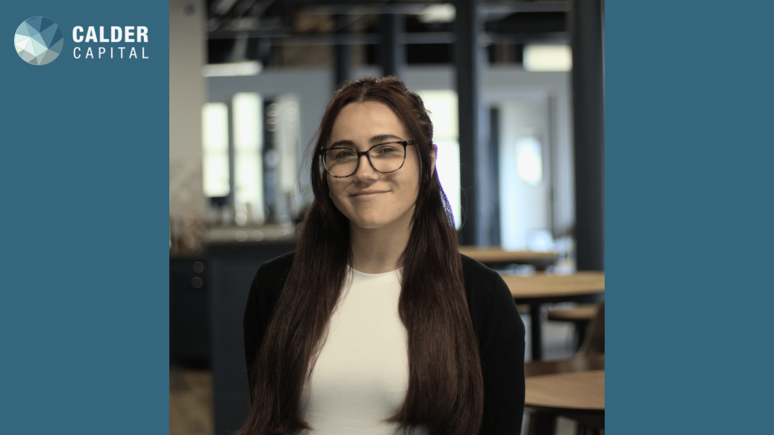 Mallory, our new office admin, smiling while standing in the office with a modern, professional background. She has long, straight hair, glasses, and is wearing a white top with a black cardigan.