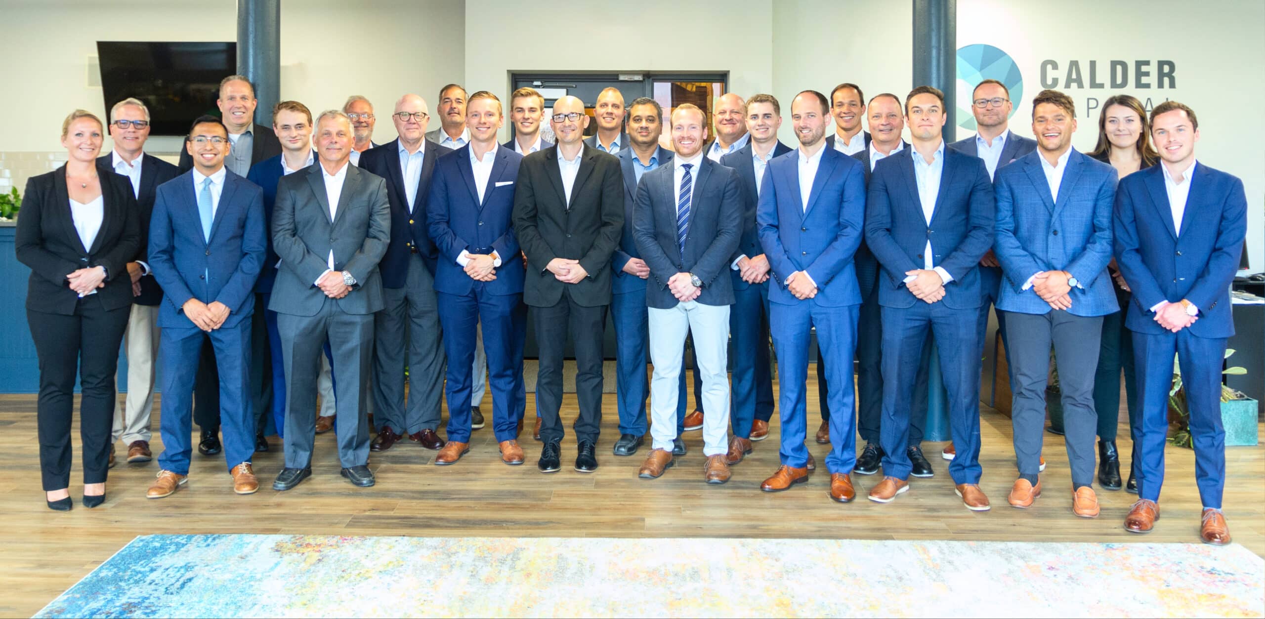 Group photo of Calder Capital team, specialists in selling mechanical and electrical businesses, standing together in professional attire at their office.